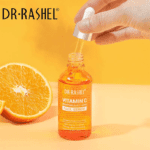 A bottle of Dr Rashel Vitamin C Serum with a dropper applicator and Orange in Background
